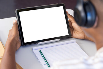 Using tablet with headphones, student taking notes in school classroom, copy space