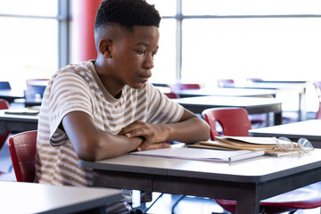 In school, boy sitting at desk with books and notepad, concentrating