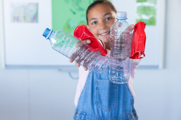 Holding plastic bottles and balloons, girl smiling in school classroom