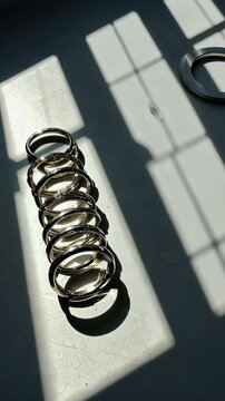 Sleek silver metal rings arranged in a row, bathed in sunlight, casting window shadows on a bright surface, creating a modern, minimalist composition.