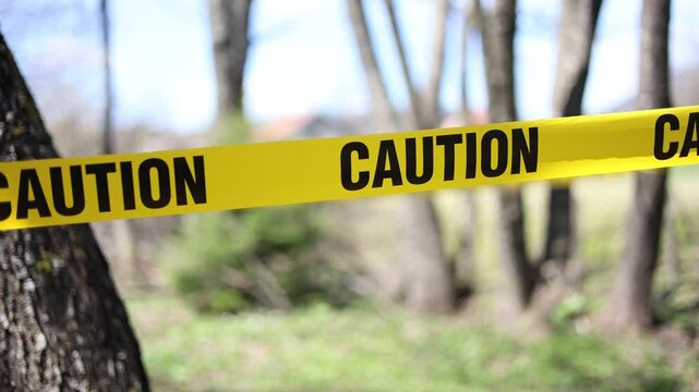 Yellow caution tape stretched across trees, blocking access to a restricted area, creating a sense of danger and warning