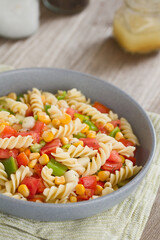 Vegan fusilli pasta salad with vegetables (tomato, cucumber, green bell pepper, sweet corn kernels)...