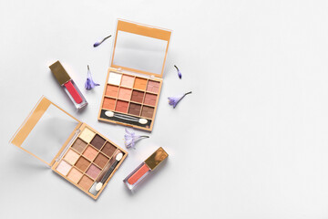 Eyeshadows palettes with lip glosses and flowers on white background