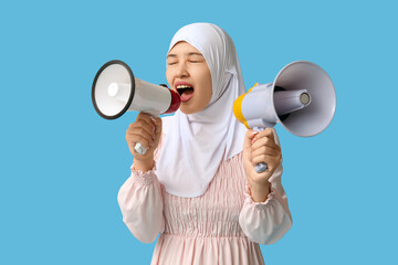 Young Asian Muslim woman shouting into megaphones on blue background. National Be Heard Day