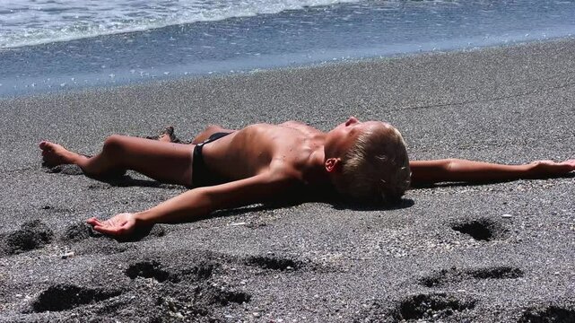 A child sunbathes on the sand of the Mediterranean Sea on the beach in Alanya. A foaming wave. Vacation by the sea. The boy lies on a small pebble under the rays of the sun.Turkey. 4K