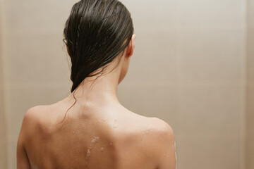 Relaxed woman with long hair enjoying a shower, water droplets on skin, serenity and self-care concept in a peaceful bathroom setting.
