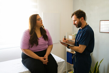 Plus-size female patient conversing with healthcare professional, taking notes during medical...