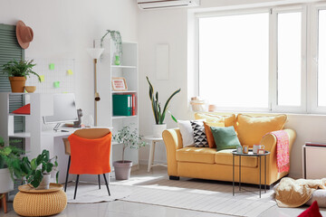 Interior of living room with workplace, computer, houseplants and yellow sofa