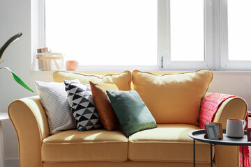 Yellow sofa, coffee table, houseplants and window in light living room
