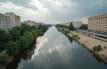 Fototapeta premium Panoramic view of Orenburg city embankment along Ural river. Buildings, green trees reflect in water. Summer cityscape, peaceful scenery. Architecture, urban environment, travel destination.