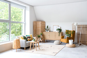Interior of light living room with grey sofa, armchair and drawers