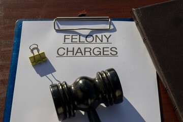 A felony charges paper secured in a clipboard, placed with a gavel resting on the desk, symbolizing...