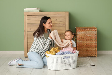 Young woman and her daughter sort through fresh laundry near green wall at home