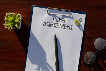 Legal document titled “Plea Agreement” placed neatly on a clipboard set on the desk with pen,...