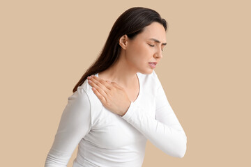 Young woman suffering from pain in shoulder on beige background