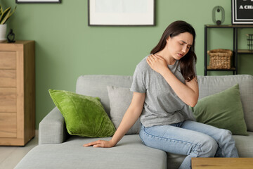 Young woman suffering from pain in shoulder on sofa at home