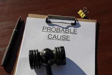 A probable cause document rests in a clipboard beside a gavel on a wooden desk, representing the documentation needed for court-authorized action.
