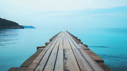 Obraz premium Wooden pier extends into calm blue sea with land visible in the distance.