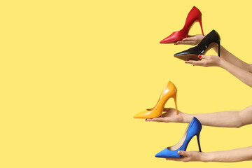 Female hands holding different heels on yellow background