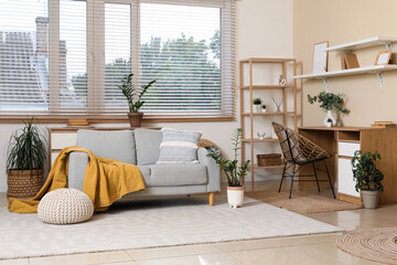Interior of stylish living room with grey sofa, window, workplace and houseplant