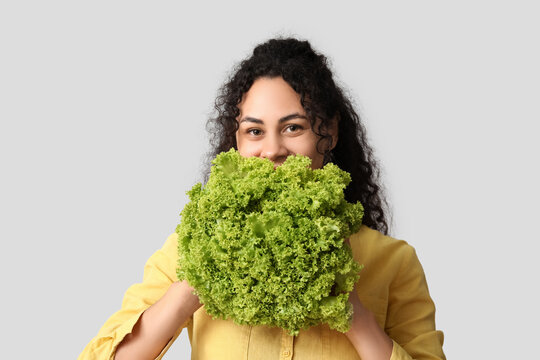 Young happy African-American woman with fresh salad on grey background. Independence from Meat Day - Powered by Adobe