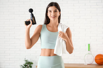 Fototapeta premium Sporty young woman with percussive massage device in gym