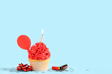 Sweet Birthday cupcake with burning candle and party whistle on blue background