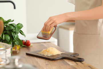 Young woman grating cheese on wooden cutting board in kitchen