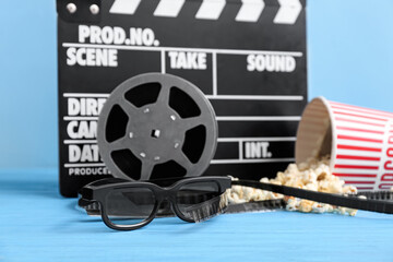 Movie clapper with popcorn, glasses and film reels on blue background