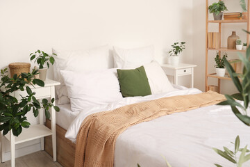 Interior of cozy bedroom with big bed, bedside tables and many different houseplants