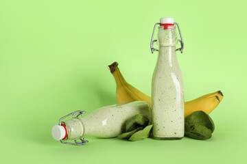 Bottles of fresh spinach smoothie with banana on green background