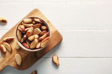 Bowl and board with tasty Brazil nuts on white wooden background