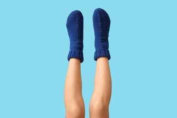 Legs of young woman in blue knitted socks on color background