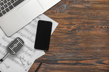 Music sheets with laptop, mobile phone, earphones and microphone on wooden background with space...