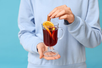 Young woman holding glass cup of hot mulled wine on blue background