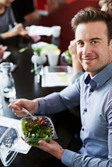 Meeting, eating and portrait of businessman with salad in office for team building lunch for collaboration. Food, smile and male designer with colleagues enjoying healthy meal in workplace.