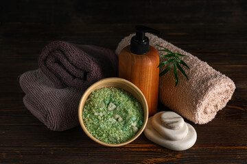 Plakat Bottle of cosmetic product, sea salt, spa stones and clean towels on dark wooden background