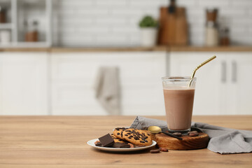 Glass of sweet chocolate milk and plate with tasty cookies on wooden table in kitchen