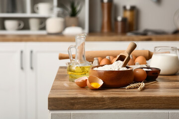 Bowl of flour with eggs, scoop, jug of milk and oil for preparing dough on kitchen counter