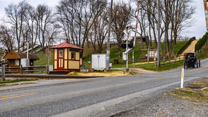 A quaint rural train crossing features vintage structures and winding paths amidst trees, inviting visitors to explore the area's natural landscape.