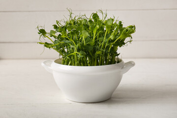 Bowl with fresh micro green on light wooden table