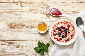 Composition with tasty oatmeal, syrup and berries on white wooden background