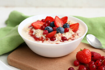Bowl with tasty oatmeal with berries on white background, closeup