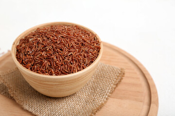 Wooden board with bowls of raw brown rice on white background