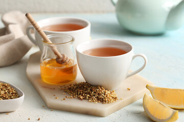 Cups of hot buckwheat tea, jar with honey and lemon slices on light background