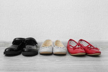 Different girl's shoes on floor near white wall