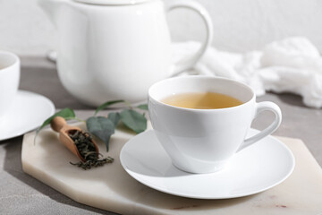 Cup of hot green tea and dried leaves on grey table
