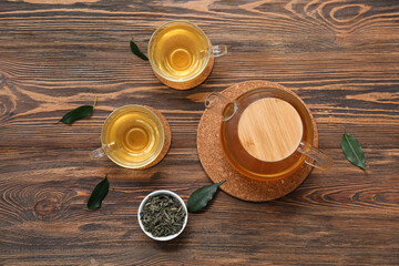 Glass cups and teapot of hot green tea with dried leaves on wooden background