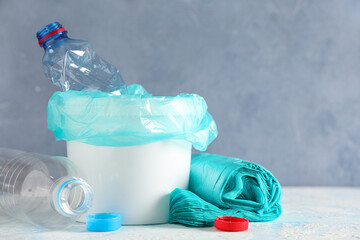 Bucket with garbage bags, plastic bottles and caps on color background