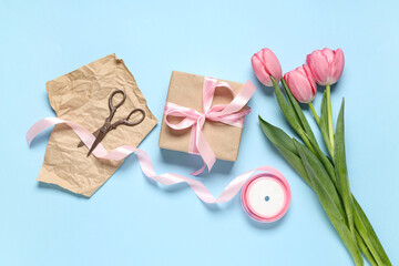 Gift box with tulips, wrapping paper and ribbon on blue background. International Women's Day